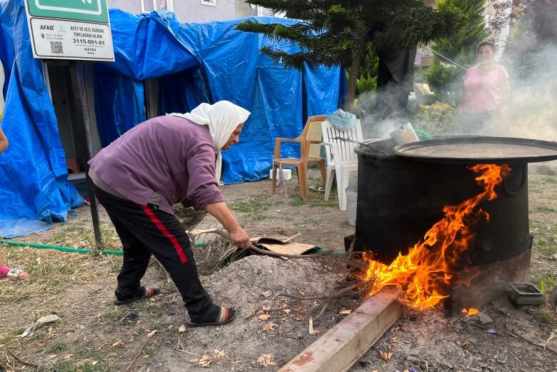 A woman tends over a fire that is heating a large basin of water.