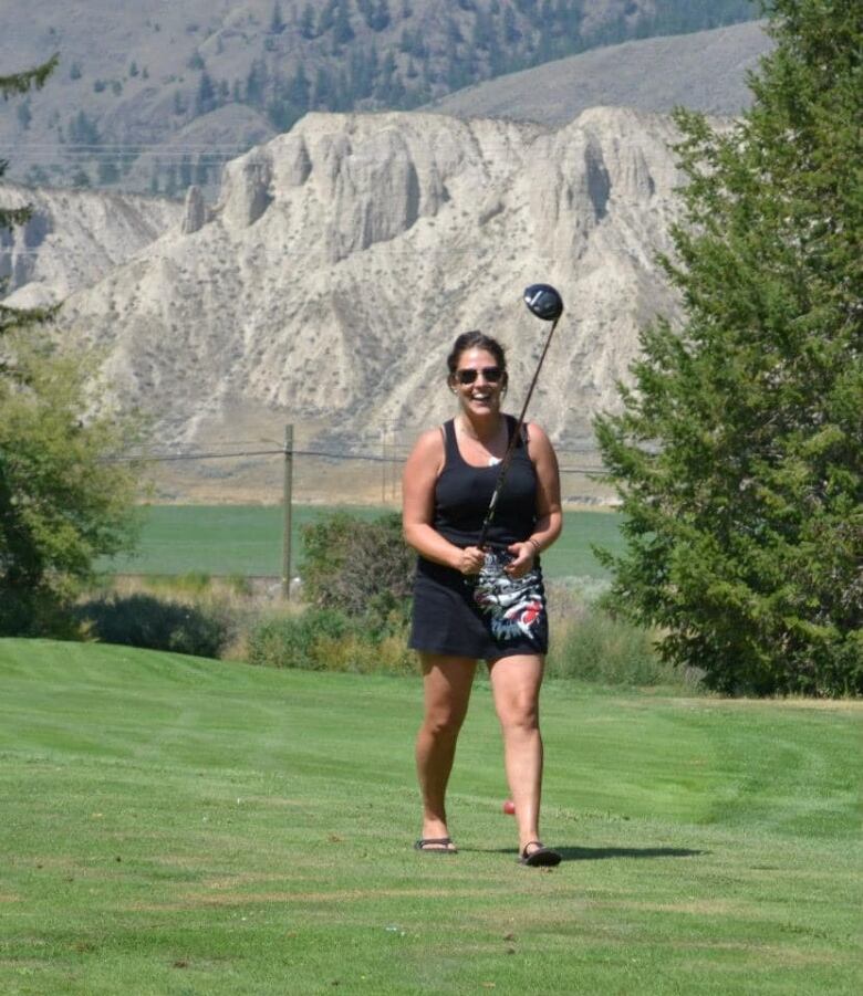 A woman walking across a gold course smiling.