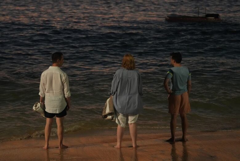 Three people stand in shallow water, their backs to the camera.