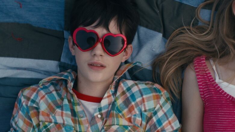 Still frame from the film Before I Change My Mind. Overhead shot of Vaughan Murrae wearing heart-shaped sunglasses.