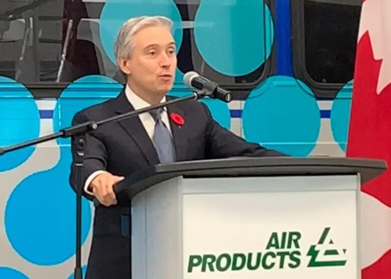 Middle aged man speaks at a lectern in front of a bus. 