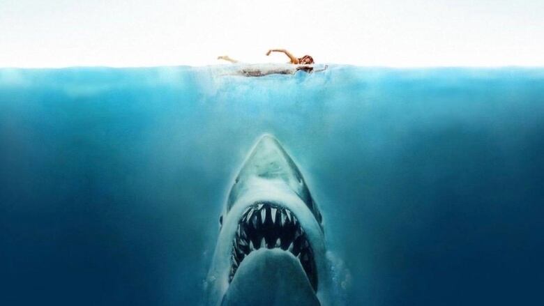 Promotional poster for the film Jaws. A shark lurks below the surface with its mouth open wide as an unsuspecting woman swims above.