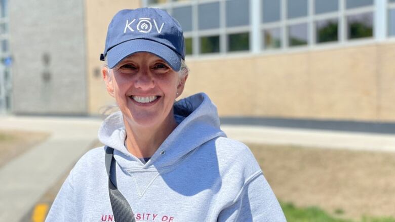 A smiling woman, wearing a baseball hat and hoodie.