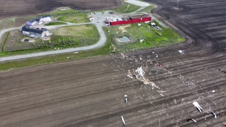 Debris is splayed across an open field from a large storage building that is near a pair of homes