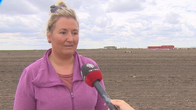 A woman in a pink zip-up sweater stands in an open field