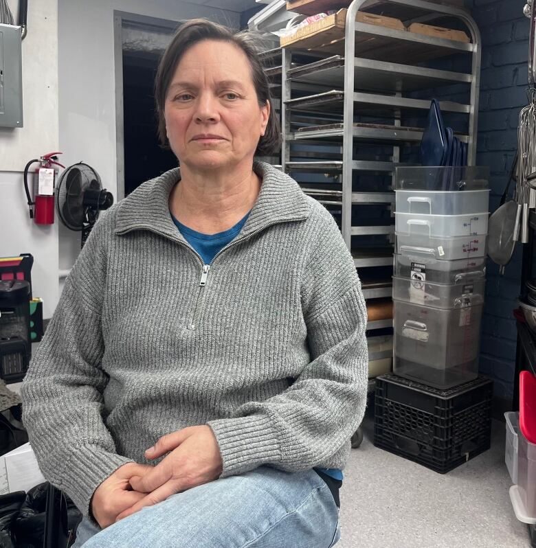 A close-up of a woman sitting down in a kitchen space. She has a serious look on her face.