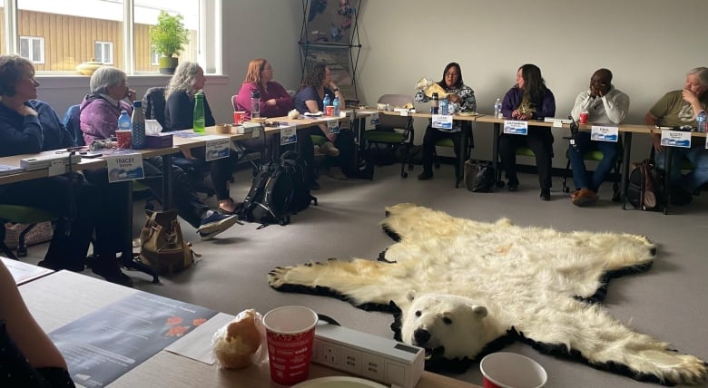 A group of people sit around a table with a polar bear rug in the centre. 