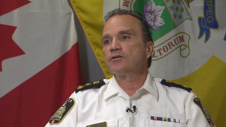 A man in a police uniform is pictured in front of a Canada flag and a Manitoba flag.