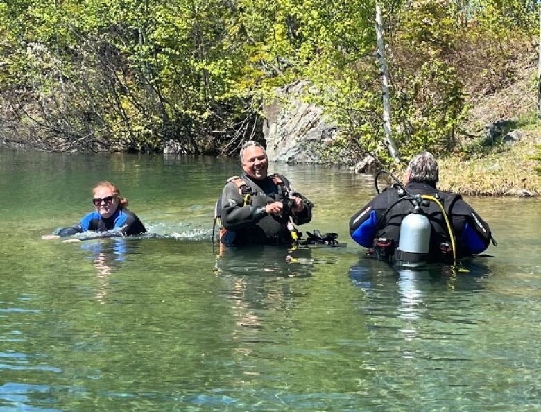 A woman and two men in a body of water, wearing scuba gear.