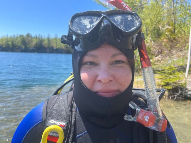 A close-up of a smiling woman, wearing scuba gear.