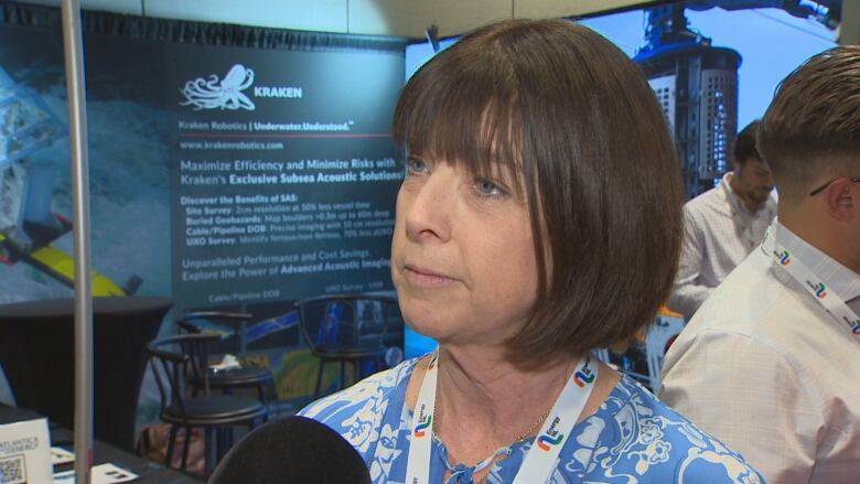 A woman with short brown hair, blue eyes and wearing a blue dress. There's a lanyard around her neck.