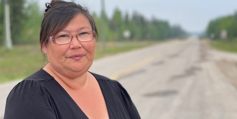 Woman in black shirt and glasses stands on rural road.