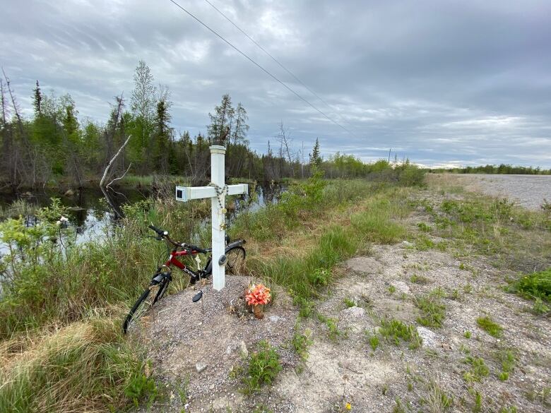 White cross on grass with beads on it, bike. 