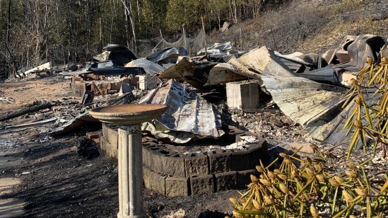 A bird bath stands in from of a pile of ash and rubble where a house once stood.