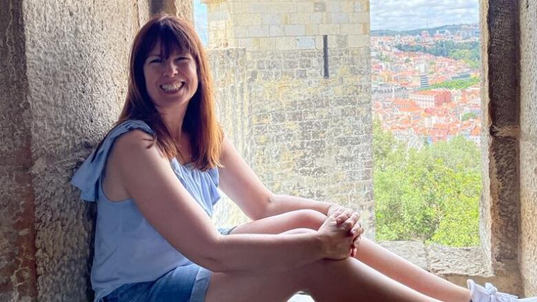 Smiling woman sits in the window of a tower in Lisbon, Portugal.