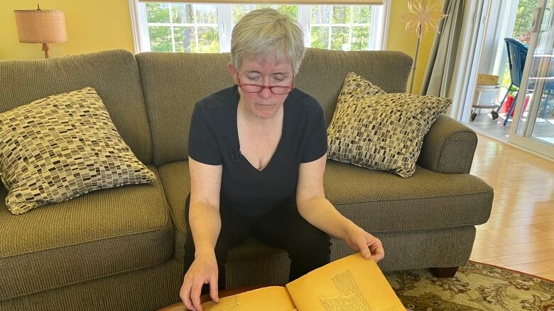 A woman sits on the couch looking at an old scrapbook. 