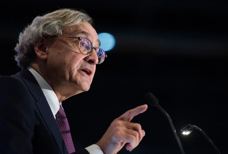 Grey haired man speaks into microphone, profile shot.