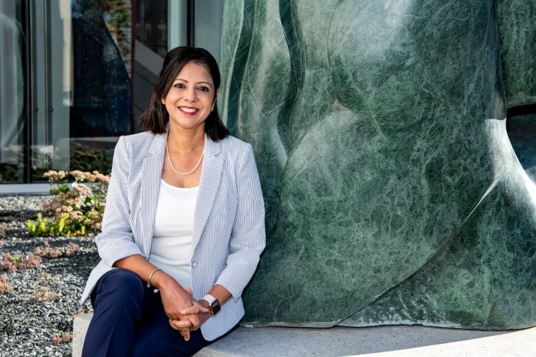 A woman in a light blue and white blazer is seated for a photo.