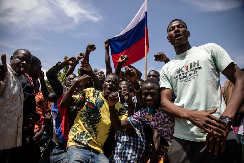 A Russian flag is held up above a crowd of young men raising their fists.