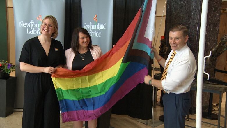 Three people stand together holding a pride progress flag.