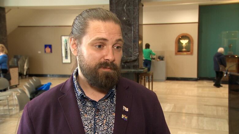 A man with his hair tied in a bun and a beard stands inside Confederation Building.