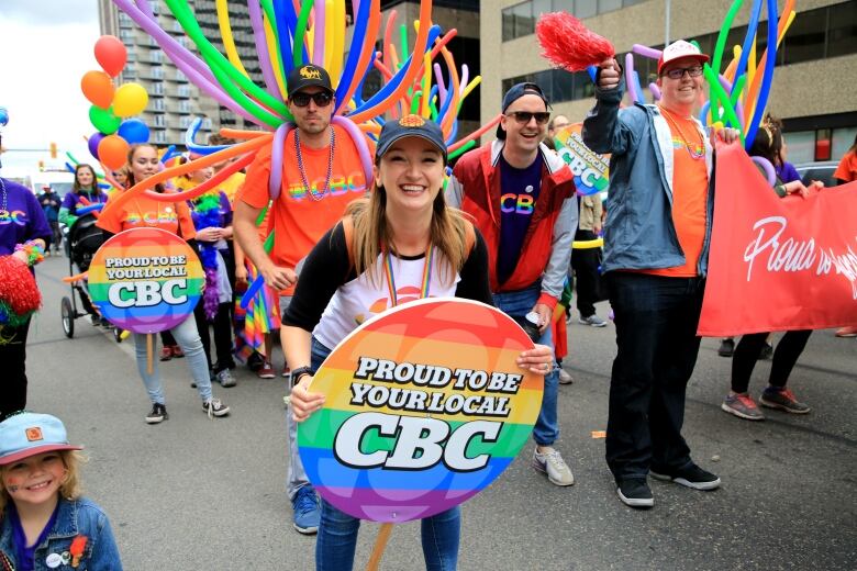 Several people in a pride parade, there are several displays of the rainbow in view.