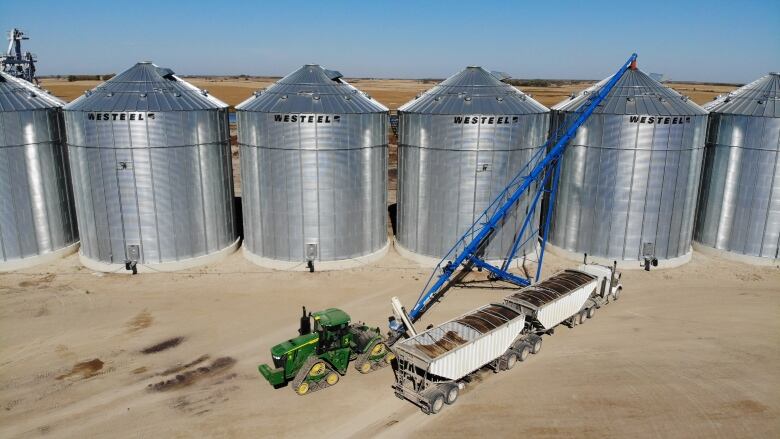 A wide shot shows grain going into a bin via a large auger.