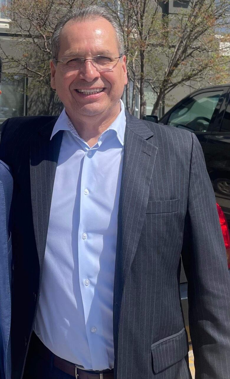 A man smiles as he's pictured wearing a blue dress suit and dark suit. 