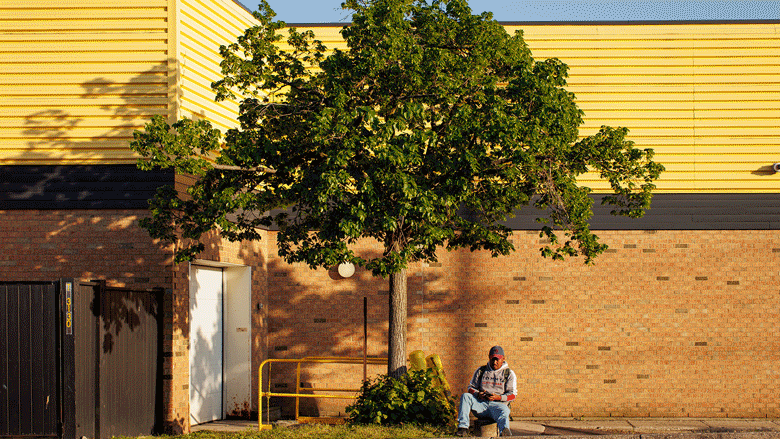 A gif of four stills shows a migrant farmer waiting for a bus outside a mall; a migrant worker perusing boxes of donated supplies at a church; an open palm holding a U.S. dollar that's been folded into a heart shape; and two men embracing one another inside a church.