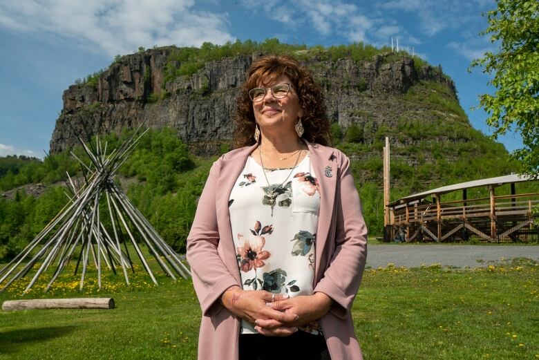 A woman stands for a portrait in a sunlight day in front of a mountain.