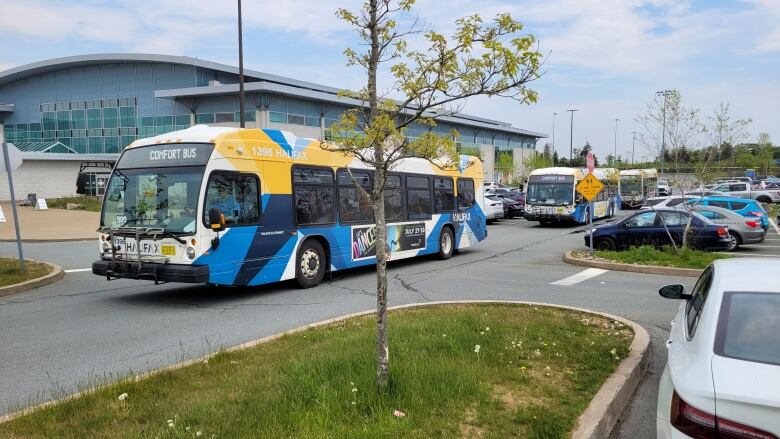 Two city buses are shown driving out of a parking lot, with an athletic center in the background.