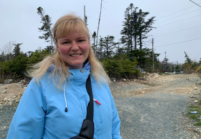 A blonde woman standing outside wearing a blue jacket smiles for a photograph.