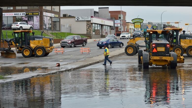 A large pool of water underneath a bridge has city workers and vehicles around it.