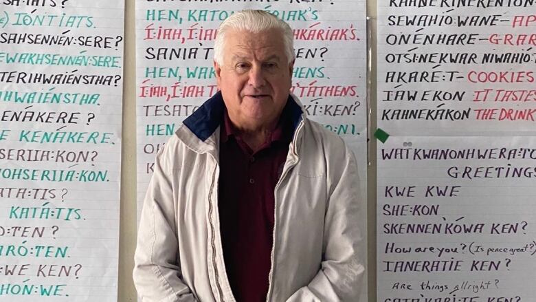 A man stands in front of taped up posters of Kanien'kha writing.