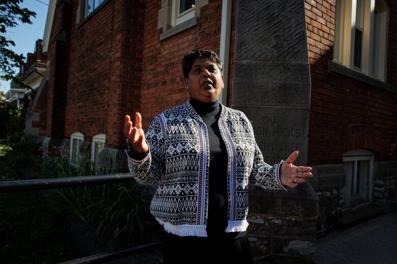 A woman stands outside an Anglican church during the golden hour on a sunny May evening.