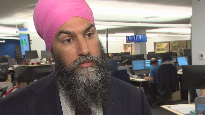 A man in a bkue suit and a pink turban standing in a newsroom.