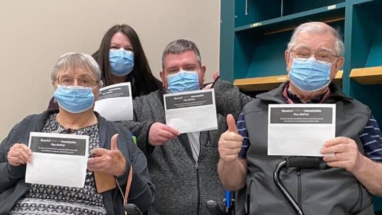 An older man and woman and younger man and woman, all wearing medical masks and giving a thumbs-up.