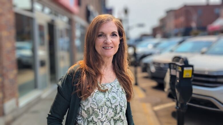 A woman wearing long hair and a sweater stands on a downtown sidewalk. 