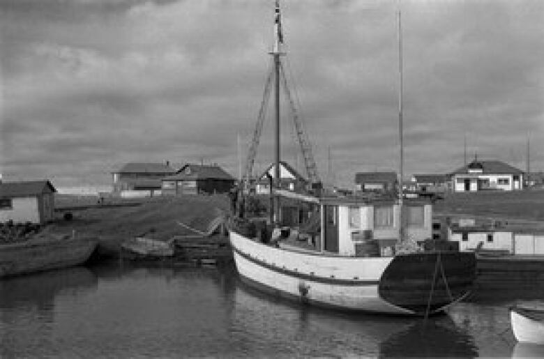 A black and white photo of a sailing ship docked at an Arctic village.