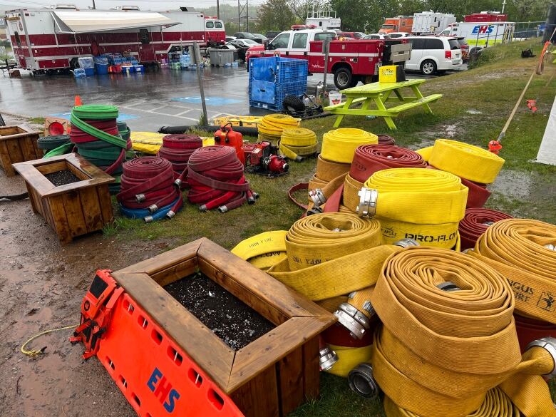 Red and yellow fires hoses sit in the rain near a parking lot. Fire trucks can be seen in the background.