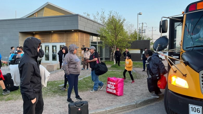 People hold luggage and bags after exiting a yellow school bus.