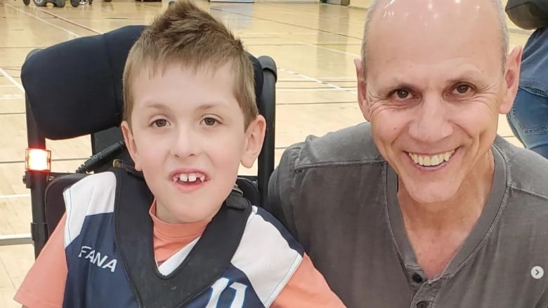 Malik Trpanier, a nine-year-old Quebec boy living with spinal muscular atrophy, smiles beside his grandfather, who is 66.