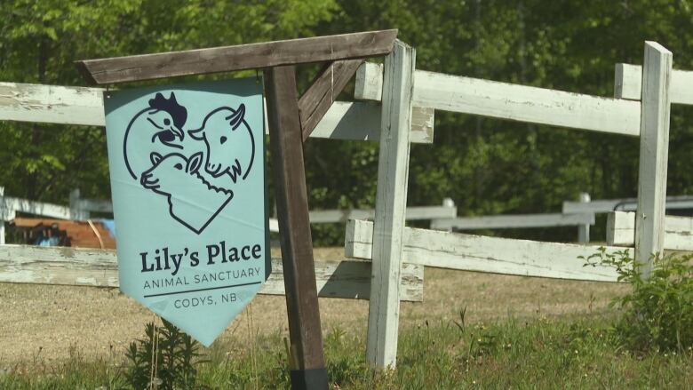 A vinyl sign handing from a wooden post that has a chicken, a goat and a sheep on it. It reads 