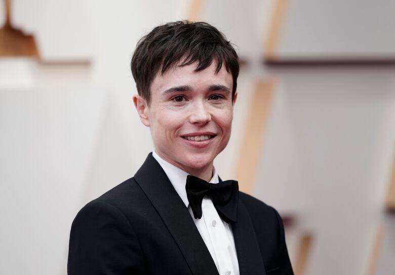 Individual with short dark hair, wearing a black tux and bowtie, smiling