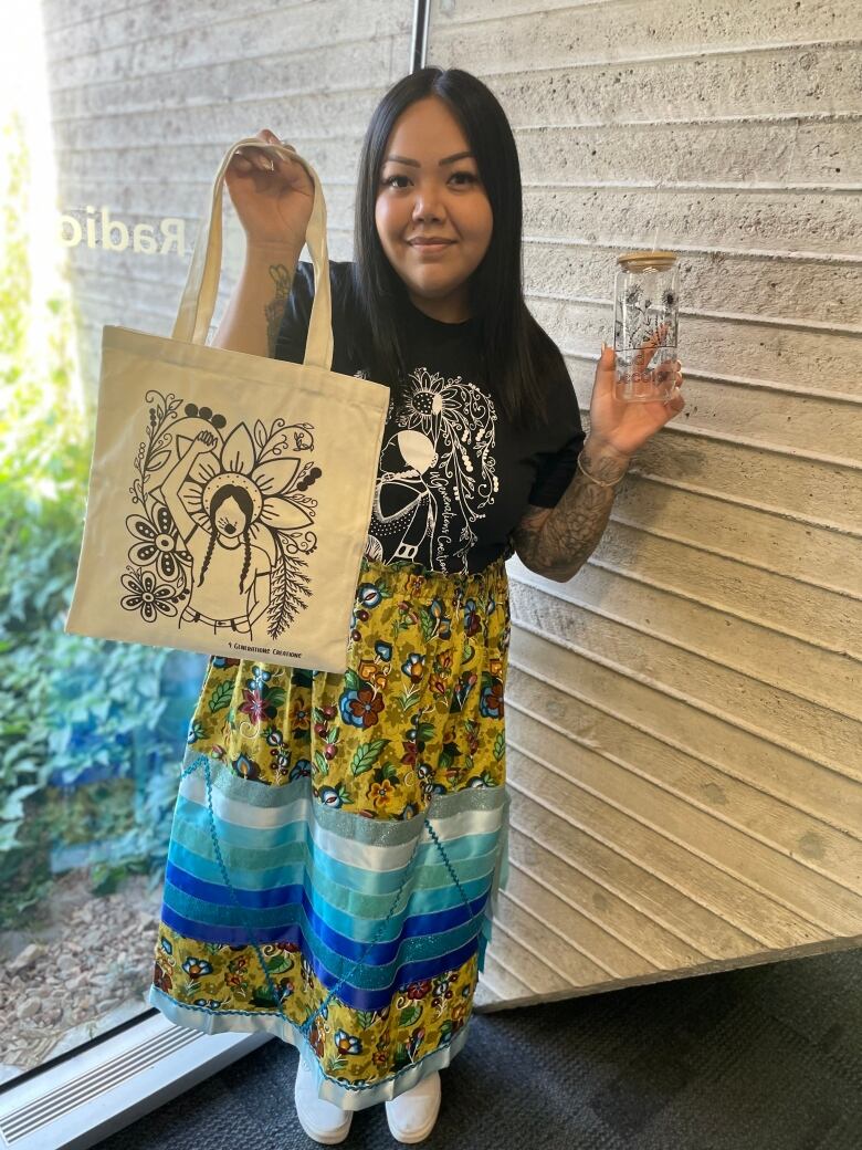 A woman stands holding a tote bag and a clear water bottle. 