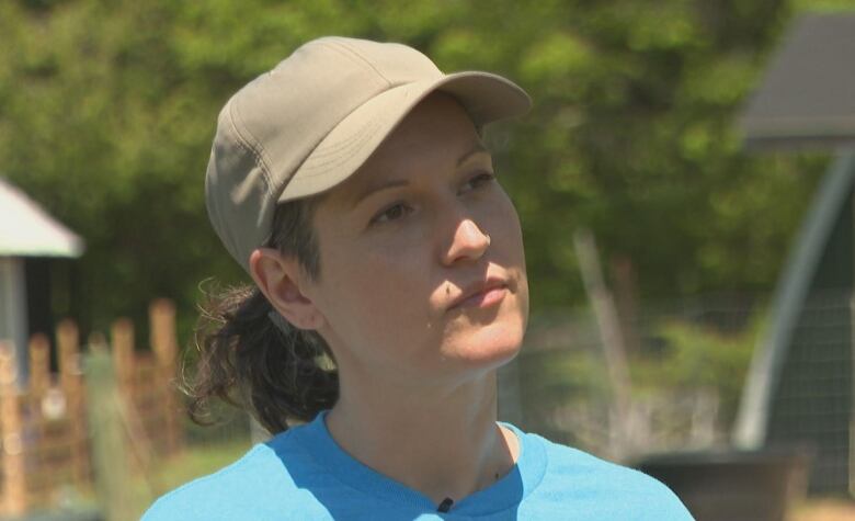 A woman with a beige hat and her hair in a ponytail. She is wearing a blue shirt.