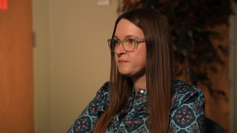 A woman with long, brown hair and glasses sits in a boardroom.