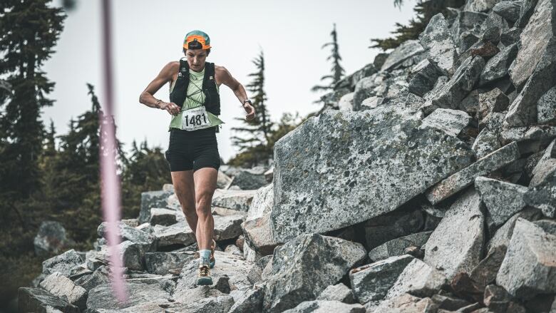 A woman wearing racing gear runs down a rocky mountain face.