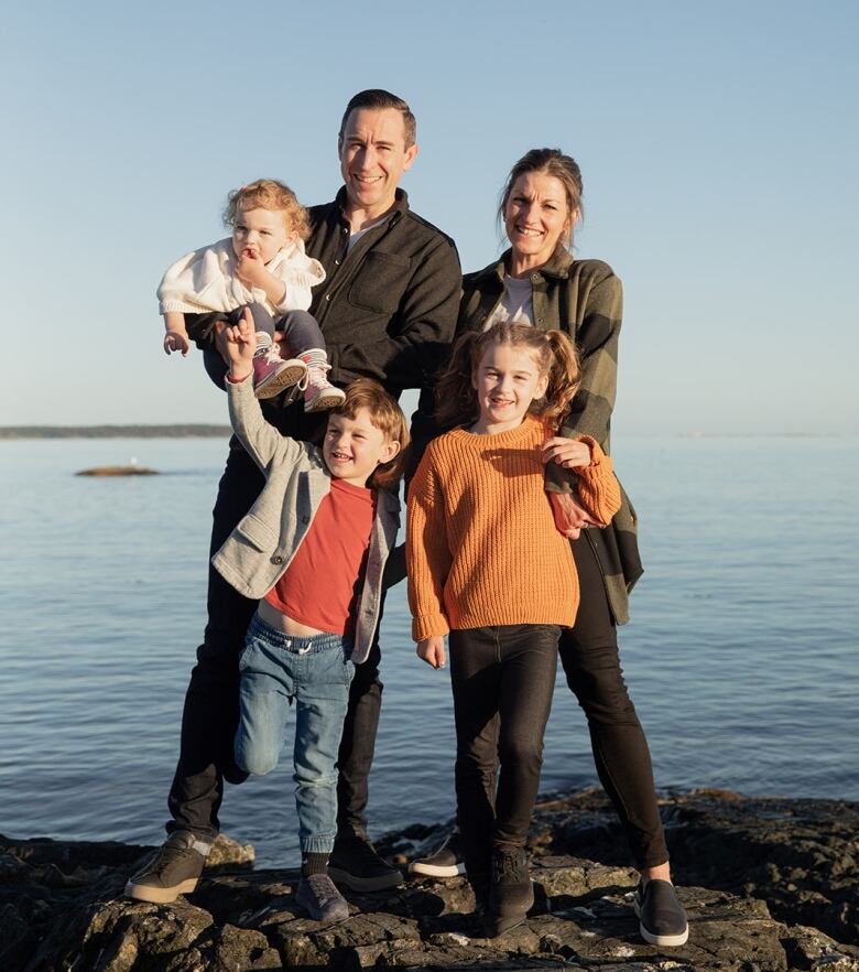 A family of five poses on a rock with the ocean visible behind them.