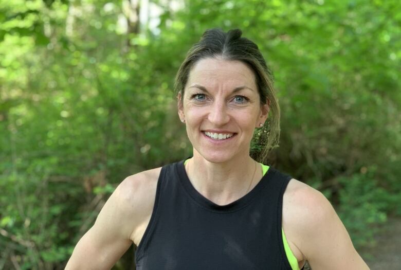 A woman wearing athletic gear with her hair in a ponytail poses for a photo and smiles.